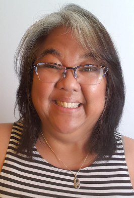 Tina is a brown-skinned woman with black and white shoulder-length hair, wearing colorful half-rim glasses and a striped black and white sleeveless top, smiling at the camera and against a plain, white background.