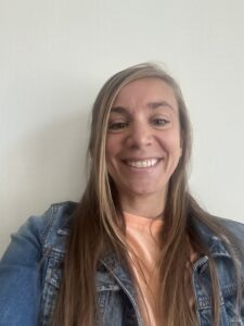 A photo of Amanda Hetzel with her hair down wearing an orange shirt and jean jacket over the top against a white background.