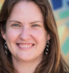 Deidre Headshot: A person with long, light brown hair and long earrings smiling at the camera.