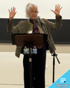 Tsehaye stands in front of a mic and podium speaking with her hands in the air.