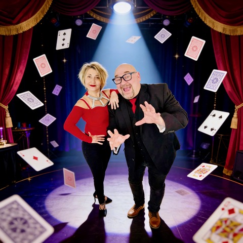 Photo of Magic Morgan & Lilian posing in a spotlight with cards flying around them.