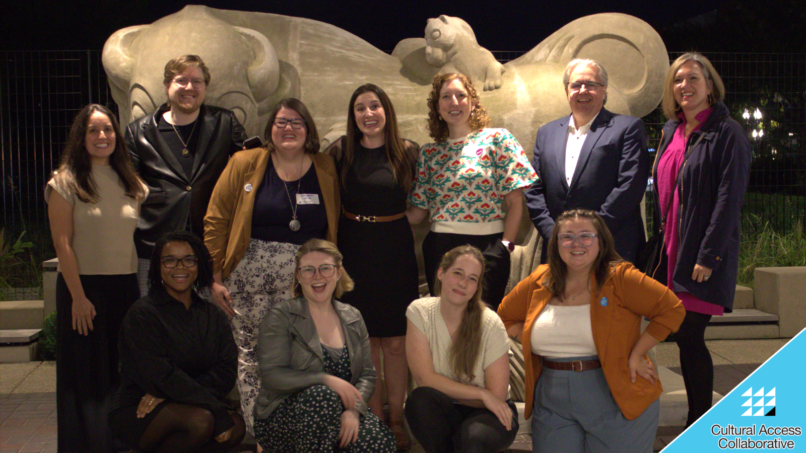 Current and former members of the board and Steering Committee pose in front of a bull statue smiling at the camera.