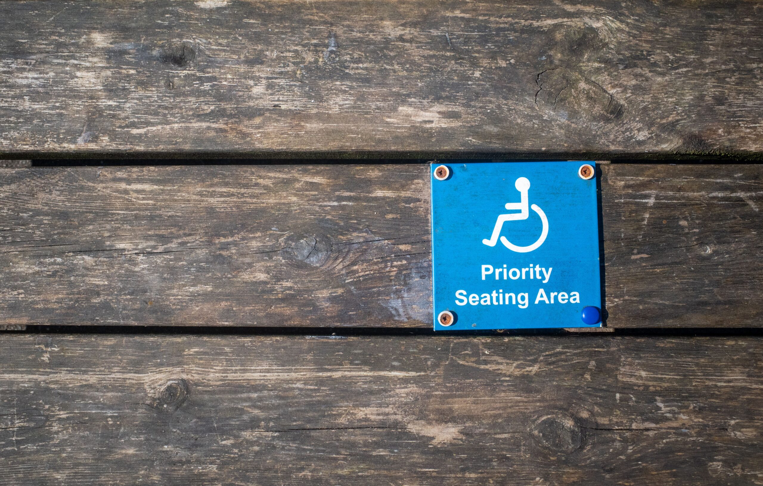 Stock photo of wooden table with metal plaque that shows a person in a wheelchair reading 
